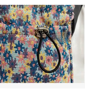 Detailed macro view of floral woven crossbody bag featuring metal drawstring buckle and cord