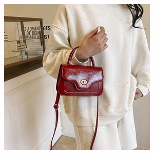 Detail of a dark red patent leather handbag with gold metal twist lock and top handle