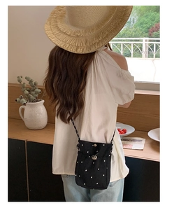 Détail d'un mini sac bandoulière noir à fleurs avec cordon sur un fond esthétique estival