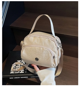 Detail of a beige nylon handbag featuring multiple zipper pockets and a metal logo