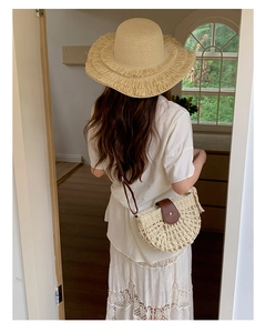 Detail of hollow woven straw bag with leather strap and matching beige fringe sun hat