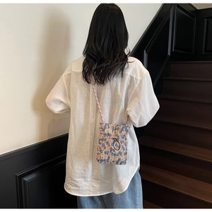 Floral crossbody phone bag with drawstring and pink braided strap worn on a white shirt