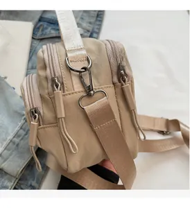 Detail of beige nylon crossbody bag with three zipper compartments and gunmetal hardware