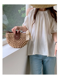 Close-up of semi-circle woven straw bag featuring a brown leather flap and lace bow detail