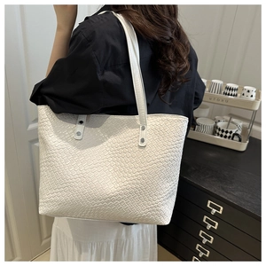 Close-up of white woven PU leather tote bag with silver rivets and leather shoulder strap