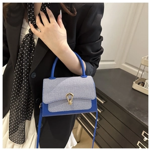 Detail of stylish mini square bag with blue leather trim and golden clasp on model