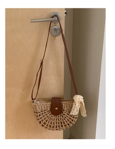 Detail of hollow woven straw bag with dark brown leather strap and lace bow decor