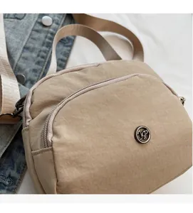Detail view of khaki nylon crossbody bag with dual zippers and metallic circular logo