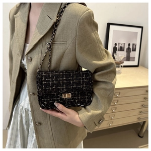 Close-up of black tweed crossbody bag with gold chain strap and metallic lock on suit