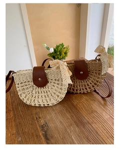 Detail view of woven straw shoulder bag with leather flap and lace bow decoration