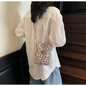 Floral drawstring crossbody phone bag with woven strap worn by model on wooden stairs
