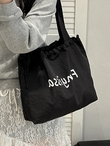 Large black drawstring nylon tote bag with white logo print worn as a crossbody bag