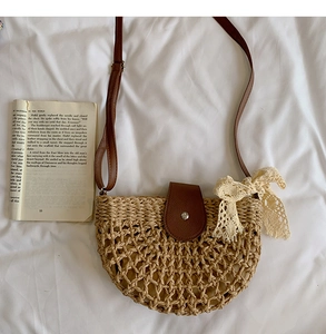 Detail of woven straw semi-circle bag with lace bow and brown leather strap on white cloth