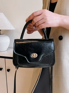 Minimalist black pleated handbag with a gold oval twist lock and a curved top handle