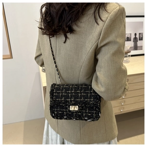 Black and gold tweed crossbody bag with chain strap worn over a stylish camel blazer