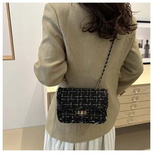 Detailed view of black tweed crossbody bag with golden chain strap on model's shoulder