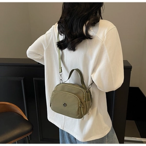 Olive green nylon crossbody bag detail showing multi-layered zippers and adjustable strap
