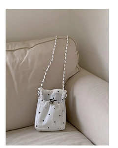 Détail du sac nuage blanc à fleurs avec bandoulière tressée noire sur un canapé