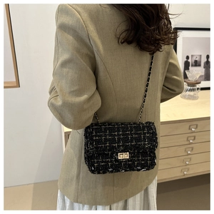 Classic black and gold tweed crossbody bag with metal chain strap worn by a model