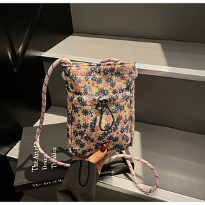 Detail of floral woven mini crossbody bag featuring adjustable drawstring and braided strap