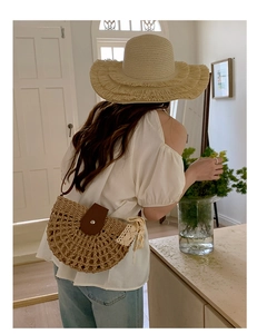 Detail of woven straw handbag featuring brown leather buckle and white lace ribbon