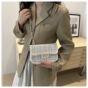Detail of tweed crossbody bag with gold chain strap worn with a beige blazer