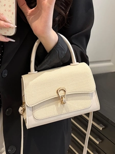 Cream-colored shoulder bag with woven flap and golden horseshoe buckle in a mirror selfie