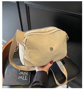 Detail of cream nylon crossbody bag with metal logo and textured fabric strap