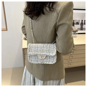 Detail of tweed crossbody bag with woven gold thread and metal chain strap on shoulder