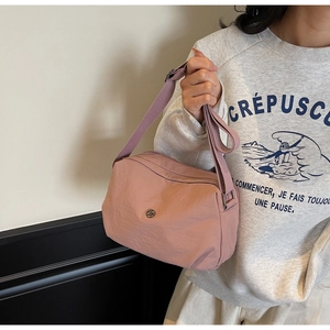 Detail of pink nylon crossbody bag with adjustable strap and circular logo on model