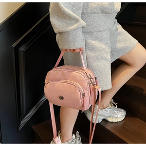 Action shot of pink nylon multi-pocket handbag worn as a crossbody bag by a model
