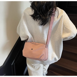 Pink minimalist crossbody bag with adjustable wide strap shown in a lifestyle street setting
