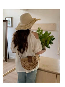 Detail of woven straw handbag with hollow mesh design and brown leather flap