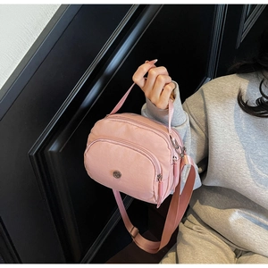Detailed close-up of pink nylon crossbody bag with multi-layer zippers and top handle