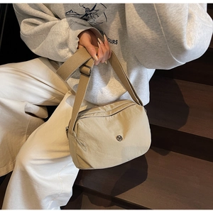 Close-up of khaki nylon crossbody bag with circular metal logo on a wooden background