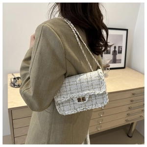Detail of tweed crossbody bag with golden chain strap and fringe edges worn by model
