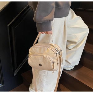 Detailed view of beige nylon crossbody bag with multiple zippers shown on a model