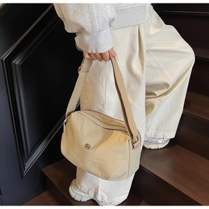 Detail of beige nylon crossbody bag with adjustable strap on model in modern staircase