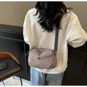 Detail view of a taupe nylon crossbody bag with adjustable wide fabric strap and round logo