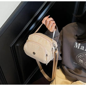 Detail view of beige nylon crossbody bag featuring multi-pocket design and wide canvas strap