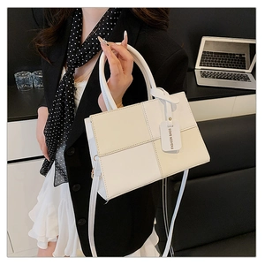 Détail du sac à main carré minimaliste crème avec surpiqûres quadrillées et étiquette mode