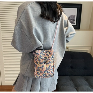 Rear view of a floral mini crossbody phone bag styled with a grey sweatshirt and pleated skirt