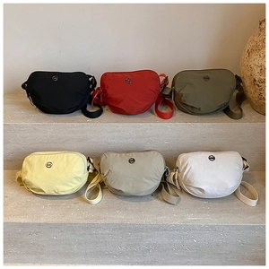Close-up of crescent nylon crossbody bags in six colors arranged on stone steps