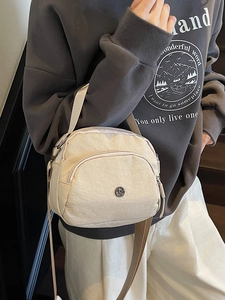 Cream nylon shoulder bag with multi-layer zippers and adjustable strap worn by a model