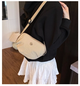 Detail of beige crossbody bag with adjustable fabric strap and round metal logo emblem