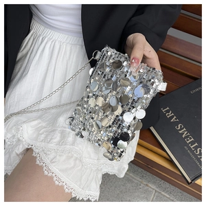 Detailed view of silver sequin crossbody bag with thin metal chain strap on vintage bench