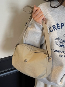 Minimalist beige nylon crossbody bag with wide fabric strap and metallic logo