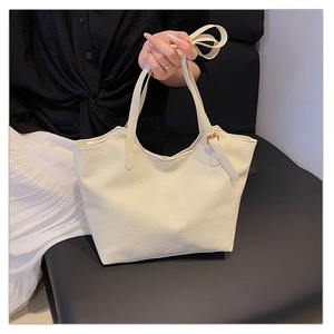 Detailed macro of cream-colored tote bag with pleated leather texture and gold metal buckle