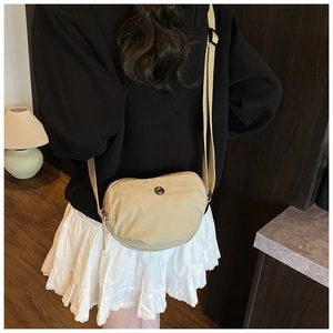Close-up of beige nylon crescent crossbody bag featuring adjustable strap and metal logo