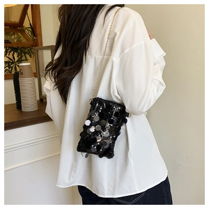 Detail of black sequin crossbody bag with gold chain strap on white shirt